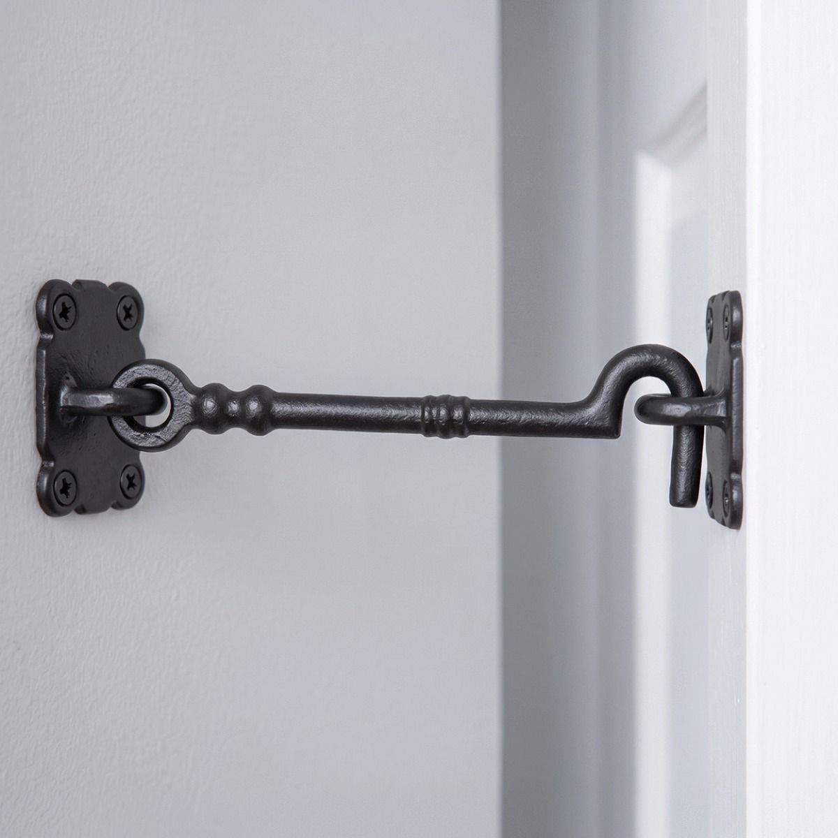 The Traditional Black Iron Large 16" Loose Ring Cabin Hook Fitted on a White Door next to a Grey Coloured Interior Wall - Digital Illustration